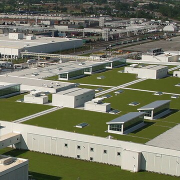 An aerial view showcases a large industrial or commercial complex with numerous white-roofed buildings and extensive parking lots, emphasizing sustainable design on a large scale